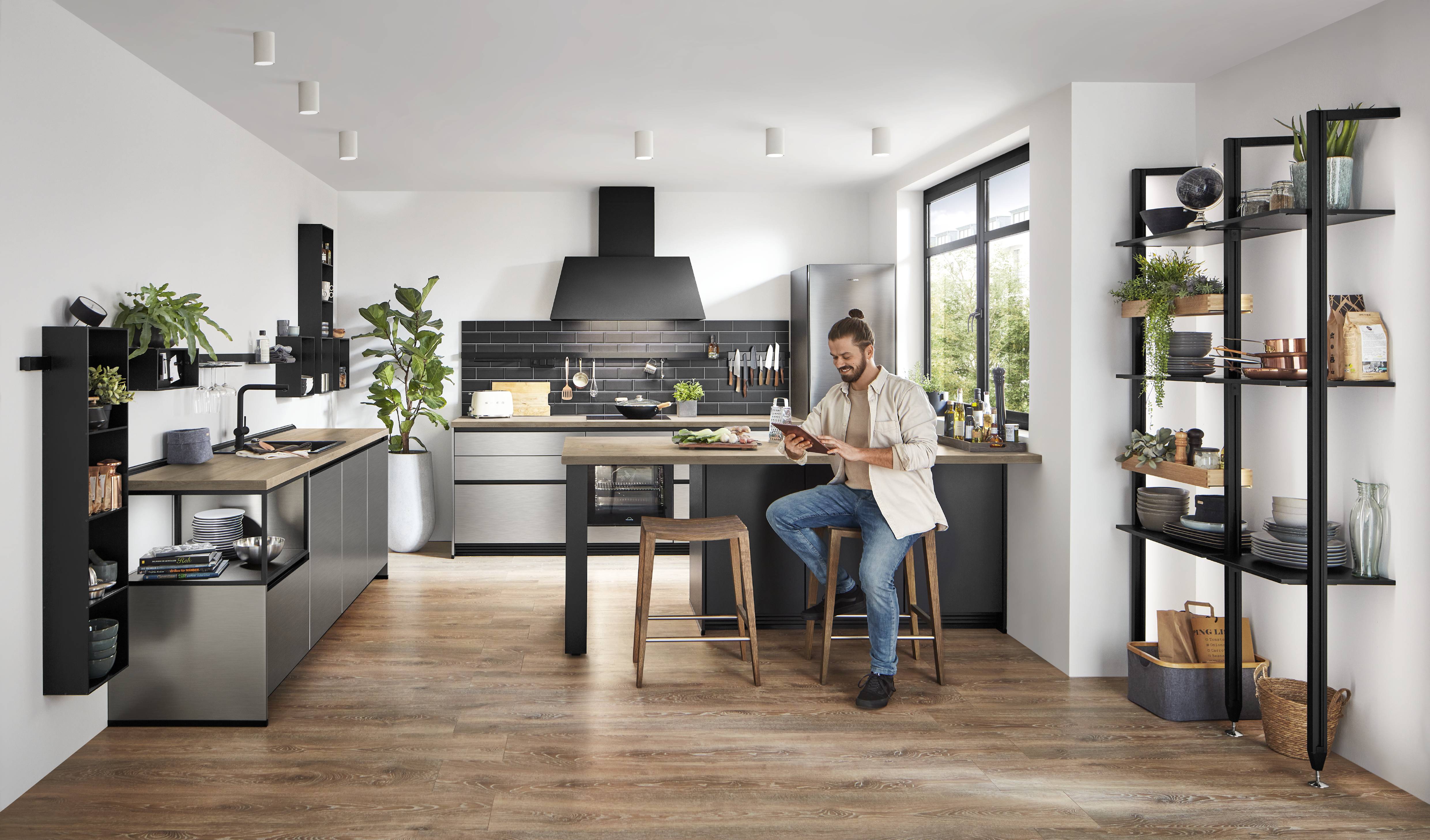 Nobilia Inox moderne Küche mit offenen Regalen Mann sitzt an Theke und schaut auf sein Tablet